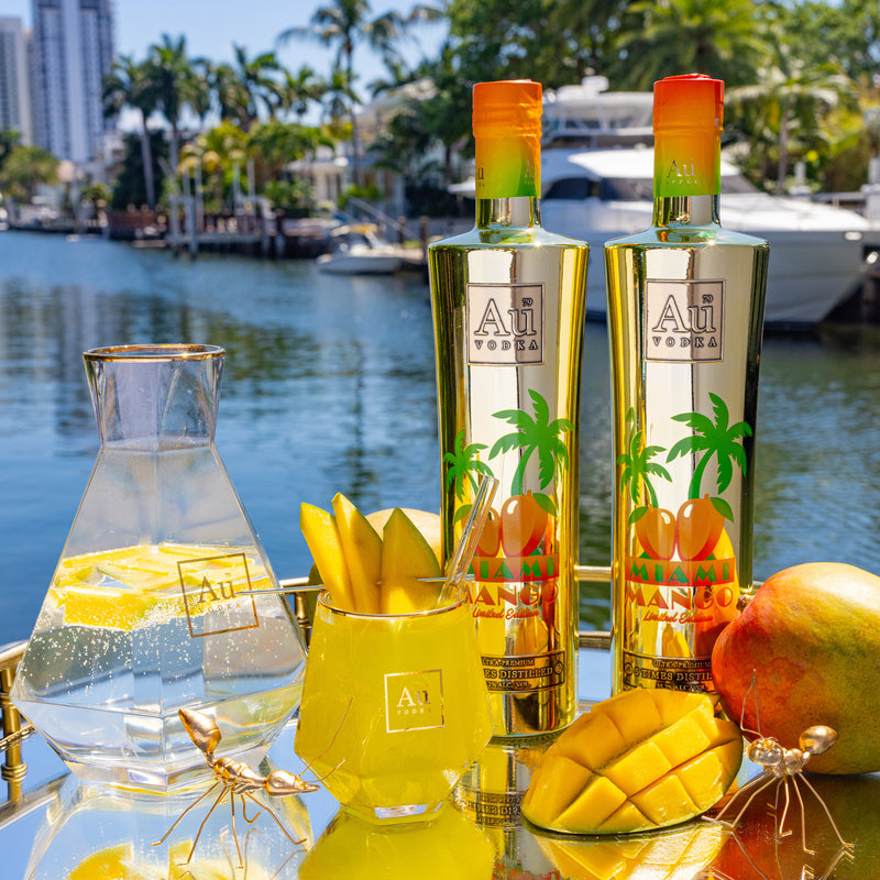 Two Au Vodka Miami Mango bottles, a pitcher of lemonade, and a glass of mango cocktail on a tray